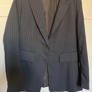 Kavaj marinblå kritstreck  - Snygg och skön kavaj i marinblått med kritstreck. Basplagg som funkar i alla år. Strl 36. Varsamt använd så den är i fint skick. Möjligtvis lite nopprig under armarna.