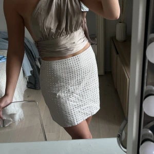 Vit/beige kjol - Fin vit/beige kort kjol med platta nitar. Passar perfekt till festkvällar men går både att klä upp och klä ner. Har använt en gång med stickad tröja vilket var superfint. Toppskick 🤍