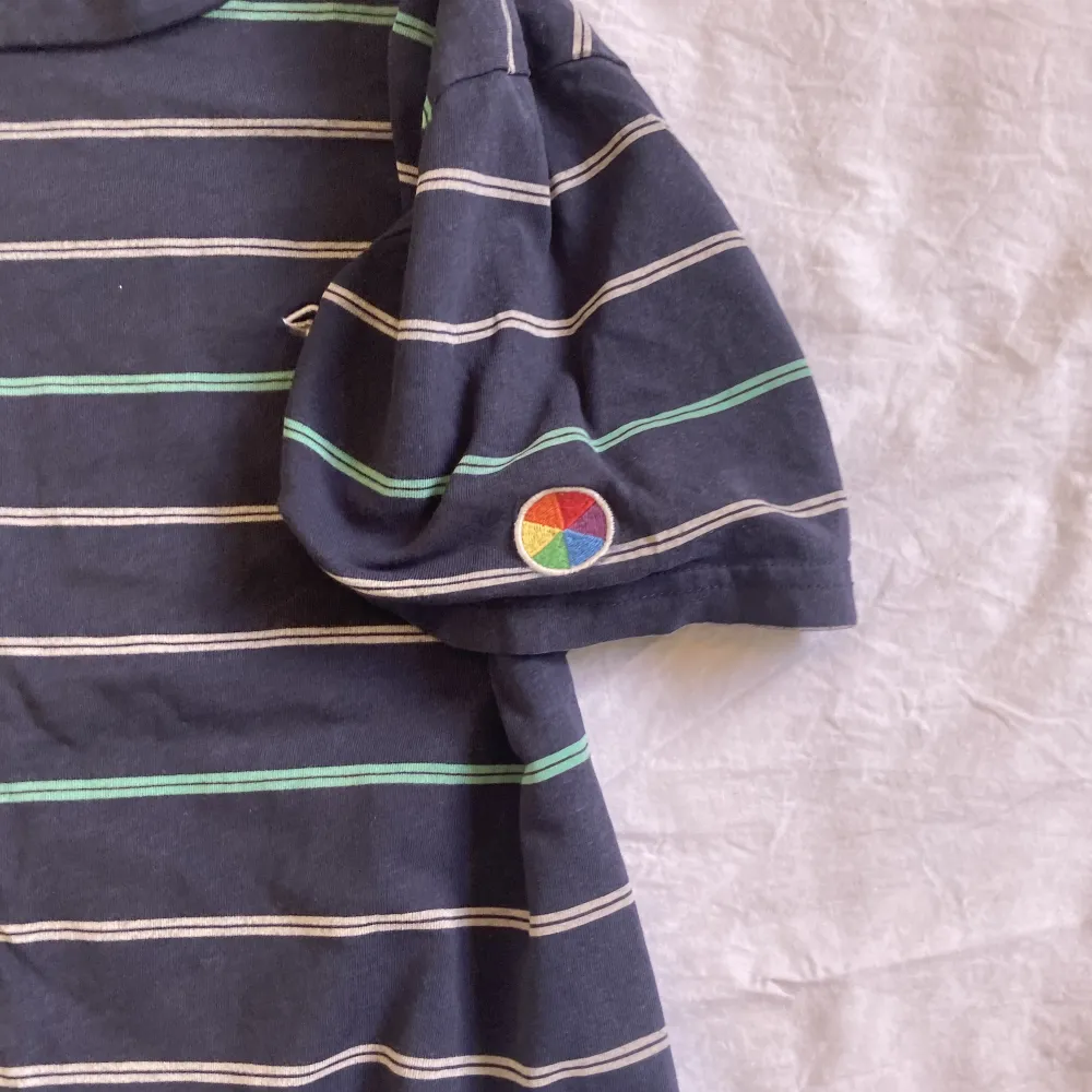 Randig holister T-shirt i storlek XS. Har en regnbågsfärgad cirkel som är broderat på vänstra ärmen. T-shirts.