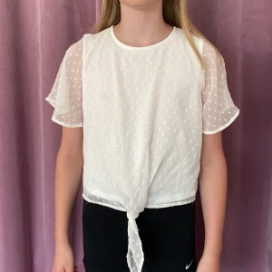Vit blus🐚🌸 - Jättefin sommarblus för barn till festliga tillfällen! Materialet är luftigt och har en innertröja runt magen och över så är det ett mesh-material med broderade prickar. Det finns även ett knyte längst ner på tröjan för att justera storlek. Knapp i nacken