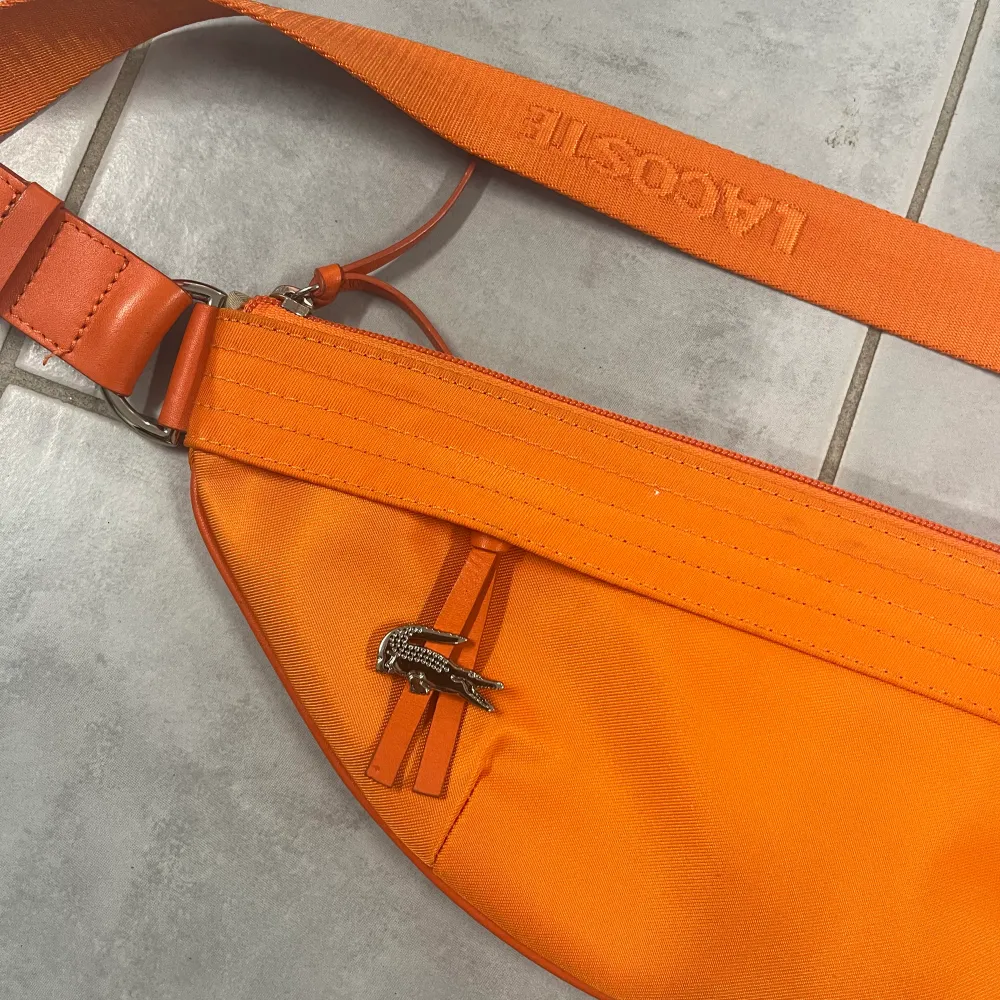 Orange väska från Lacoste i nyskick, ingenting att anmärka på. Accessoarer.
