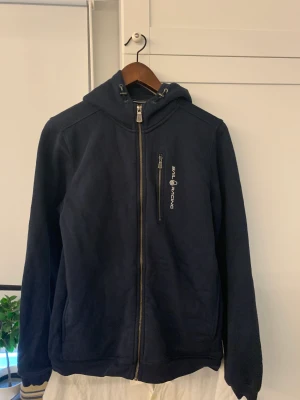 Sailracing Bowman zip Hood blå - Blå Jr Bowman zip Hood i storlek 176cm och är köpt från kidsbrandstore för 999kr och säljer den för 600kr. Anledningen för att jag säljer min tröja är för att den har blivit för stor och jag använder den inte längre