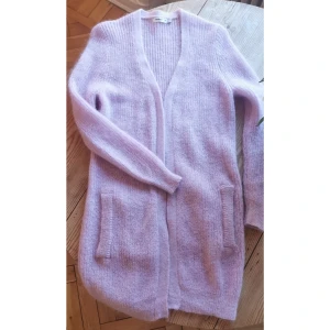 Lång kofta Mohairmix - Glesstickad ljuslila kofta i mohair med fickor. Lång modell - ca 85 cm. 32% mohair, 28% ull, 40% nylon. Handtvätt eller ulltvätt. Oanvänd