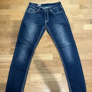 Trueys - Riktigt feta True Religion Jeans. Cond 8/10 någon söm har gått upp. Midja storlek 32/33  Total längd 107 cm  Benöppning 15 cm