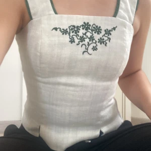 Korsettopp med gröna detaljer🩷 - Ljusbeige korsettopp med dragkedja bak och inbroderade gröna blommor fram!💕 Märket är Kaiseralm. Skicket är bra💚