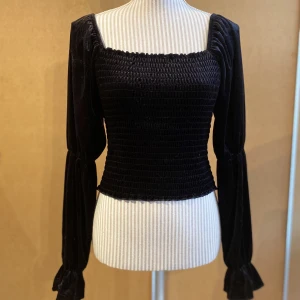 Svart blus i velour - Svart blus i velour tyg med smock på fram och baksida. Den har även lite puff i ärmarna💞säljer då jag inte använder den mer. Används några gånger och är i fint skick. Normal i storlek. 