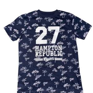 T-shirt med Hampton Republic tryck. Bakgrunden består av palmträd och någon sorts blomma. Kontakta gärna före köp. Aldrig använd i nyskick.