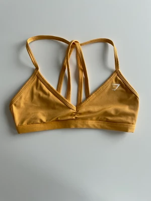 Gymshark sportbh  - Minimal sportsbra från gymshark i en gul/orange färg. Superfin men kommer inte till användning. Går att ta bort banden för en halter bra.