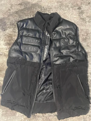 Philipp Plein  - A:A Philipp Plein väst i relativt skick.. Man ser att den silvriga färgen har försvunnit på bild 3 sen är det ihopsytt ca 1cm på ryggen men det syns inte.  Den är storlek L men passar M också.  Hämtas upp i Örebro, billigare vid snabb affär!