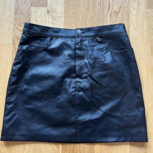 Svart kjol - Svart fejk skinnkjol i storlek 40 från H&M. Använd ett fåtal gånger och är i bra skick.