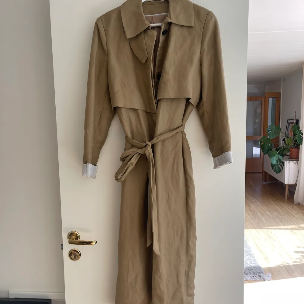 Jättehärlig trenchcoat i nyskick som förtjänar mer än att bara hänga i min garderob. Använd ett fåtal ggr. Inga defekter. Normal i storlek. Nypris 1799:- Material: 60% linne 40% viskos. Jackor.