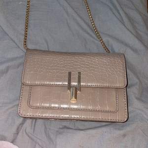 En beige/brun handväska med guld detaljer inte till användning, super fin att ha till klänning 