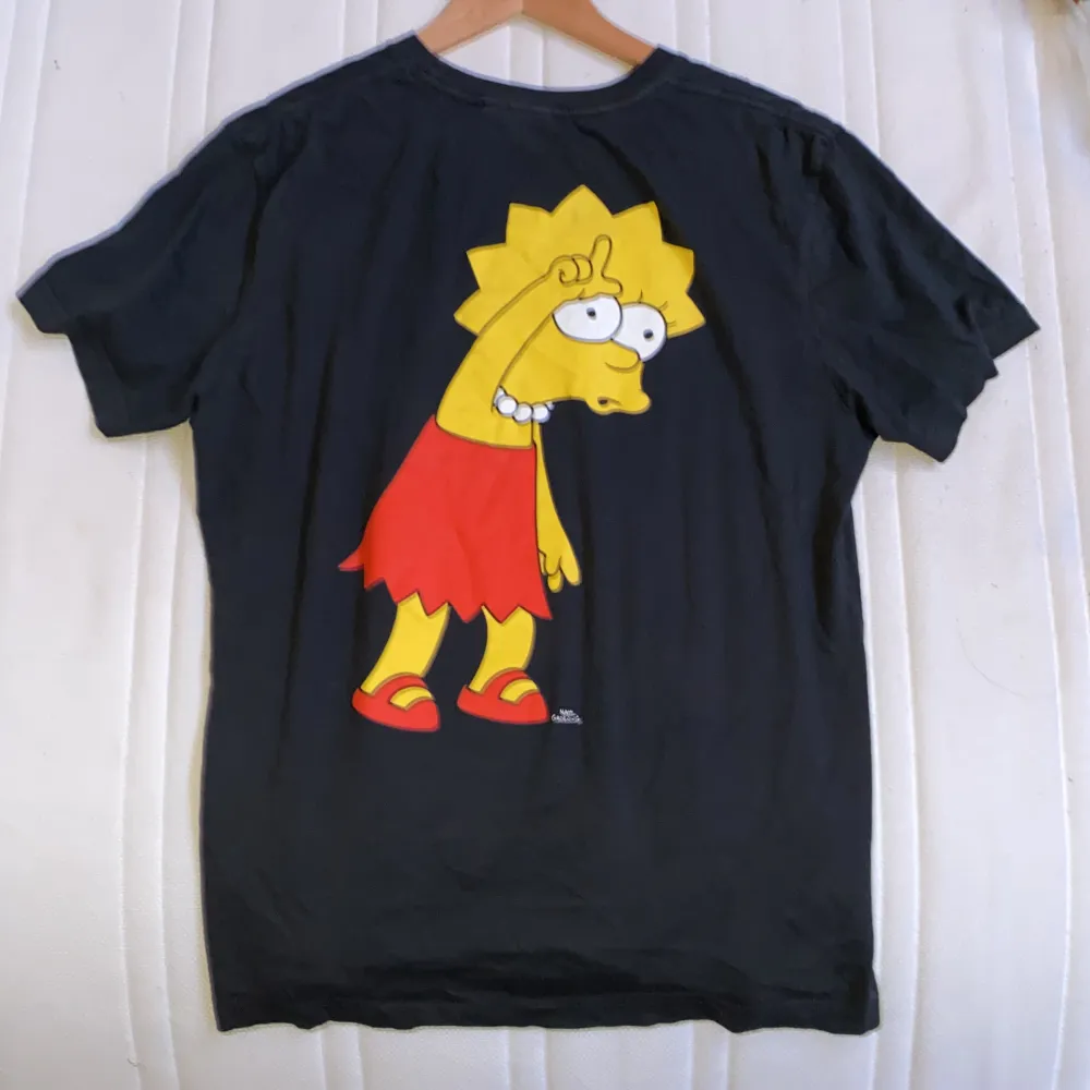 En vanlig svart t-shirt med Lisa från Simpson tryck på ryggen har aldrig varit i användning och är i en bra skick fortfarande storlek M/L. T-shirts.