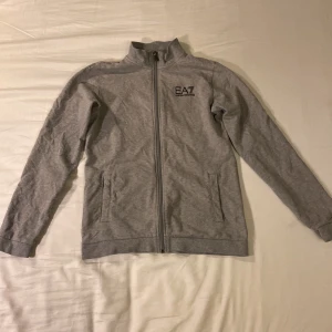 Hel Grå Emporio Armani Ziphoodie  - Det är en äkta hel grå zip hoodie från Emporio Armani som inte har några håll eller utmärkelser på sig, den har två styckna fickor på utsidan och två styckna innerfickor, den är storlek 160,  Du får budda det du vill så får jag se om det blir bra