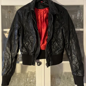 Skinnjacka  - Kaxig liten jacka från H&M med röd insida. Svart läderimitation, den är välanvänd. Strl 38. 