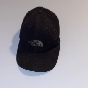 ”The North Face”-keps - En svart keps med grått märke framtill, som ni ser på bilden. Jag har ej använt denna så mycket och har inte heller någon användning längre av den och därför vill jag sälja. Storleken är justerbar.
