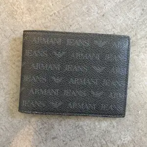 En Armani plånbok som är i svart läder med massa Armani text. Den har använts i ca 5-6 månader men kommer tyvärr inte längre till användning. Den köptes i Spanien/ Alicante i en armani butik för 99€ så ca 1000kr. säljer den nu för endast 449kr. skick=bra😄