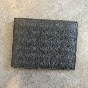 Armani plånbok - En Armani plånbok som är i svart läder med massa Armani text. Den har använts i ca 5-6 månader men kommer tyvärr inte längre till användning. Den köptes i Spanien/ Alicante i en armani butik för 99€ så ca 1000kr. säljer den nu för endast 449kr. skick=bra😄