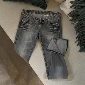 lågmidjade jeans - Lågmidjade gråa jeans med slits och nitar. Köptes på plick men aldrig kommit till användning så säljer dem igen.  Inte töjbart tyg.