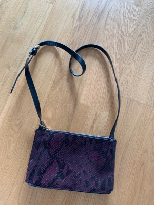 Väska från Zara - Vinröd/mönstrad väska från Zara. Crossbody bag. Två fack med dragkedja.