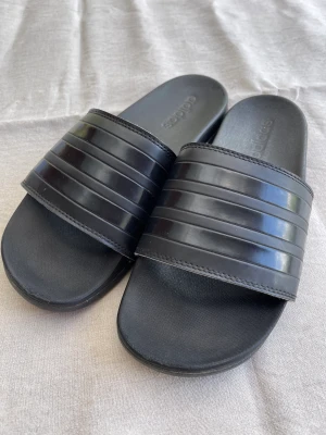 Supermjuka tofflor Adidas - Säljer mina Adidas Adilette Comfort, använda en sommar. I gott använt skick. Lite skadad framtill, se bild. Det är inget som stör alls. Dom är den mjuka modellen, som att gå på moln. Väldigt sköna. Nypris 500kr.  Köparen betalar frakten. 