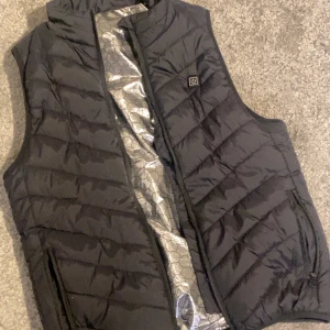 Värmeväst strl S  - Jag fick denna västen i present men är lite tight för mig.Värms upp snabbt, finns 3 styrkor på värme man kan välja mellan.Det silvriga syns inte när man har på sig den .OBS! Behöver powerbank för utomhus bruk! 