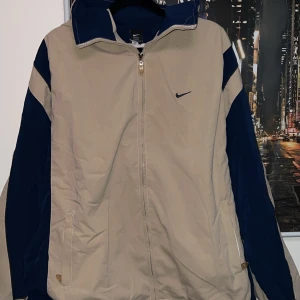 Nike Navy/Beige Vintage Jacket  - Storleken på den är S men den passar mer för M/L. S funkar om du gillar den baggy. Den är köpt från en vintage hemsida men användes aldrig p.ga den inte passade mig som S. Väldigt bra skick för en vintage tröja.