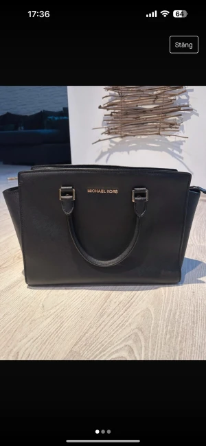 Michael Kors  - Väska från Michael Kors - Selma  Fint använt skick Många fack inuti och ett knäppe för tex nycklar Ena fästet till axelremmen har släppt lite men är limmat (bild 3)  Axelremmen medföljer (syns ej på bild) och det går att använda den som vanligt trots lim