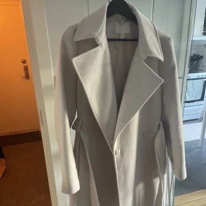Lång kappa - Lång kappa i färgen beige från H&M. Använd fåtal gånger.  Perfekt till hösten då den är lite tjockare. 