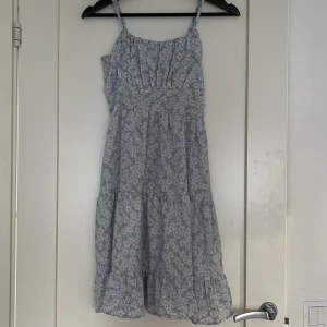 Blåblommig klänning - En jättefin och somrig klänning i blommönster. Nypris: 300kr. Där bak i ryggen finns resår och på sidan finns en dragkedja, dragkedjan syns inte alls när man har på sig den. Knälång. Säljs eftersom den är lite stor för mig och är använd 2 gånger.