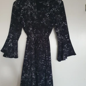 Fin klänning till vardags och fest. - Fin klänning med svart bakgrund och grått/vitt mänster med knyte i midjan som kan användas både till vardags och fest. Endast använd i ett fåtal ggr så i fint skick.