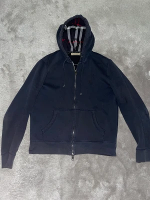 Burberry hoddie - En mörkblå burberry hoddie som är köpt från heatnlux, den är i storlek m och har inga defekter förutom hålet på bilden. Väldigt fint skick om man bortser hålet. Hoddien är äkta enligt heatnlux men har inget annat till den.