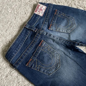 Vintage True Religion jeans - Lågmidjad och bootcut modell med snygga detaljer, de är avklippta längst ner. ❤️ Innerben: 80cm, midja rakt över: 37-38cm. Jag är 165cm som referens, kan fixa fler mått. 🫶Håll koll på min profil, lägger för det mesta upp vintage jeans! 😍