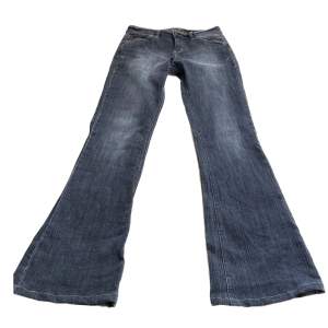 Grå/svarta utsvängda jeans med låg midja. Cool detalj på bakfickan.  Mått: innerbenslängd: 83 cm Midja: 39