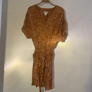 Orange Solrosklänning från Monki - Knälång vackert mönstrad klänning i strl L, perfekt till sommar tillställningar! Använt fåtal gånger men ren och utan skavanker!