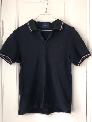 Fred Perry Piké  - nice piké från fred perry som är svart/mörkt blå. bra skick men lite blekt! 