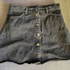 Fantastiskt fin A-linjekjol från Monki i äkta stentvättad jeans/denim.   Nypris 600 kr.  Kjolen är helt svart i verkligheten, inte alls lika ljus och ”flammig” som på bild 2 och 3 men där syns mönstret bättre.  Stängs med knappar längs hela framsidan.