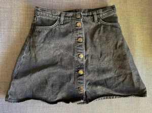 Monki, kjol strl S - Fantastiskt fin A-linjekjol från Monki i äkta stentvättad jeans/denim.   Nypris 600 kr.  Kjolen är helt svart i verkligheten, inte alls lika ljus och ”flammig” som på bild 2 och 3 men där syns mönstret bättre.  Stängs med knappar längs hela framsidan.