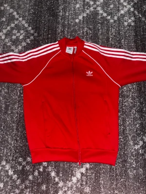 Röd adidas hoodie - Säljer min adidas zip up, då jag inte använder den längre, size M. Köpt för 900kr Använd ca 7 månader men är i samma skick som när ja köpte den.