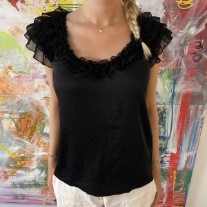 svart topp med volangdetaljer - Svart topp med volangdetaljer och i sidenmaterial! Storlek 38 och modellen är 175 cm lång! Perfekt med ett par lågmidjade jeans, kolla vår profil för det! 