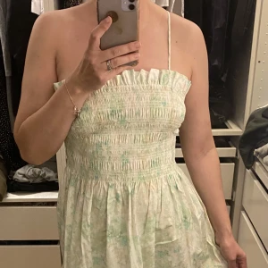 Smockklänning - Smock klänning med avtagbara axelband från H&M (helt ny) med ett fint mönster i färgerna grön, gul och vit. Storlek M.  Plagget finns i Ursvik, Sundbyberg om du önskar hämta det.