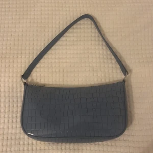En liten blå handväska! - Den blå handväskan har ormskinn material (inte riktigt ormskinn). Den kommer från h&m och är i bra skick, inga skador på den eller något! Det gör till ett längre band till den ifall man skulle vilja ha det. 