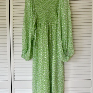 Grönblommig midiklänning med volymärmar  - Nypris: 709kr Aldrig använd, tiden för returnering gick ut. Normal i storleken, går till ca mitten av vaden. Silvriga detaljer i tyget.