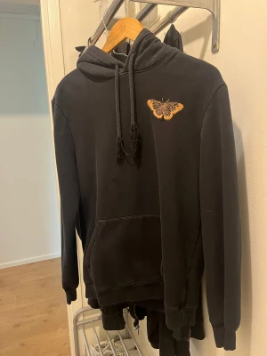 Hoodie  - En svart Hoodie med en fjäril på vänster sida. En basic Hoodie som sagt. Pris kan diskuteras, försöker bara bli av med så mycket som möjligt 