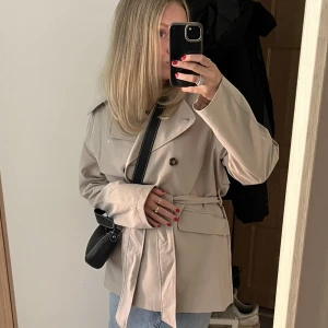 Trenchcoat  - Trenchcoat i kortare modell. Från hm i storlek S, använd ett få tal gånger. Inga slitningar eller liknande. Den är ljus Beige, färgen syns bäst på bild 1