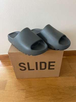 Yeezy Slide Slate Marine - Helt nya Yeezy Slide Slate Marine i storlek 43.  Köptes på CONFIRMED appen vid release.  Säljes då dom var för stora för mig.  Hämtats i Örnsköldsvik eller skickas på köparens bekostnad! 1100kr