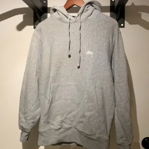 Grå Hoodie Stuzzy - Stussy hoodie i färgen grå. Passar bra nu till hösten och har en snygg passform. Köpt från SNS för 1500kr 2022. Knappt använd och är i storleken small. Meddela för andra frågor.