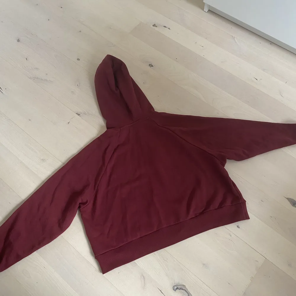 En vinröd hoodie som är lite kortare i modellen (går precis till höften). Den är mysig och ganska tunn. I bra skick och säljs då den helt enkelt inte kommer till användning så ofta 💕. Hoodies.