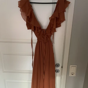 Lång brun/orange klänning - En väldigt fin lång klänning från Asos. Klänningen är aldrig använd och är väldigt stretchig. Den har knytning i ryggen och är i storlek S.