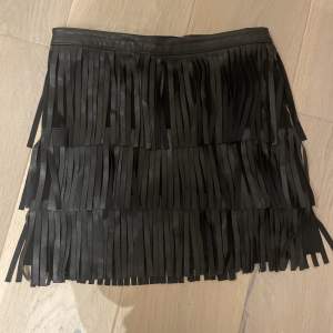 En svart, kort skinn kjol med fransar. Den är i storlek xs.